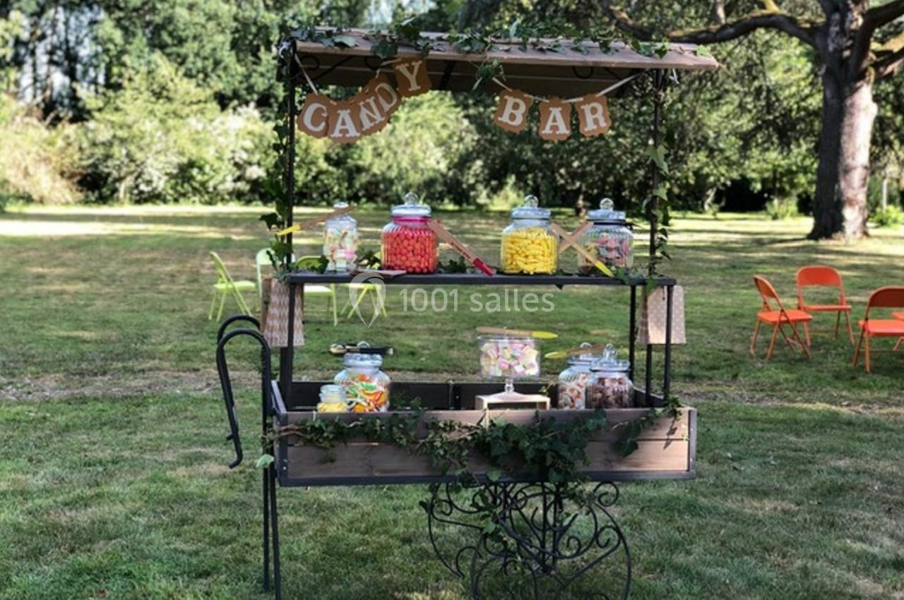 Chariot en bois décoré, rempli de bonbonnières colorées, installé sur une pelouse dans un cadre verdoyant.