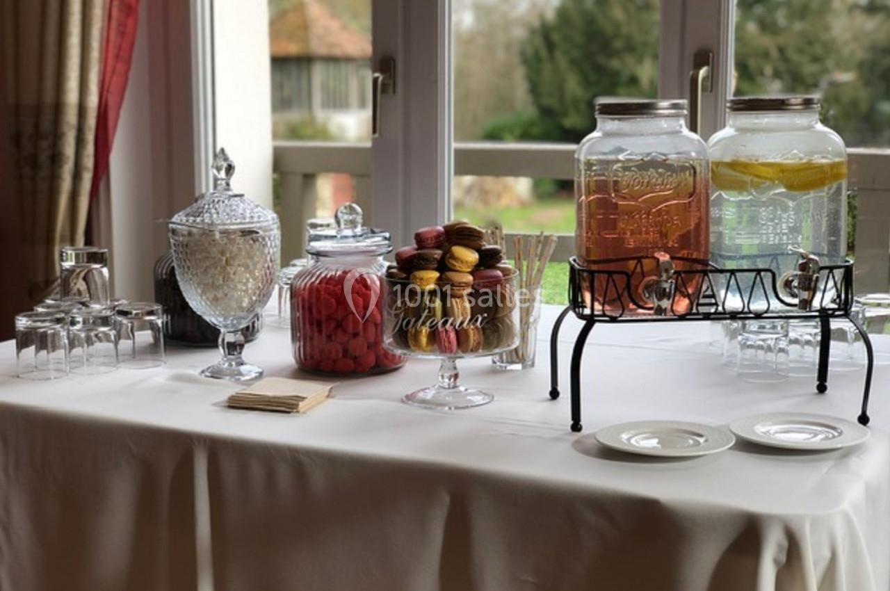 Table dressée avec des bonbonnières, des macarons, des boissons en distributeurs et des verres, près d'une fenêtre.