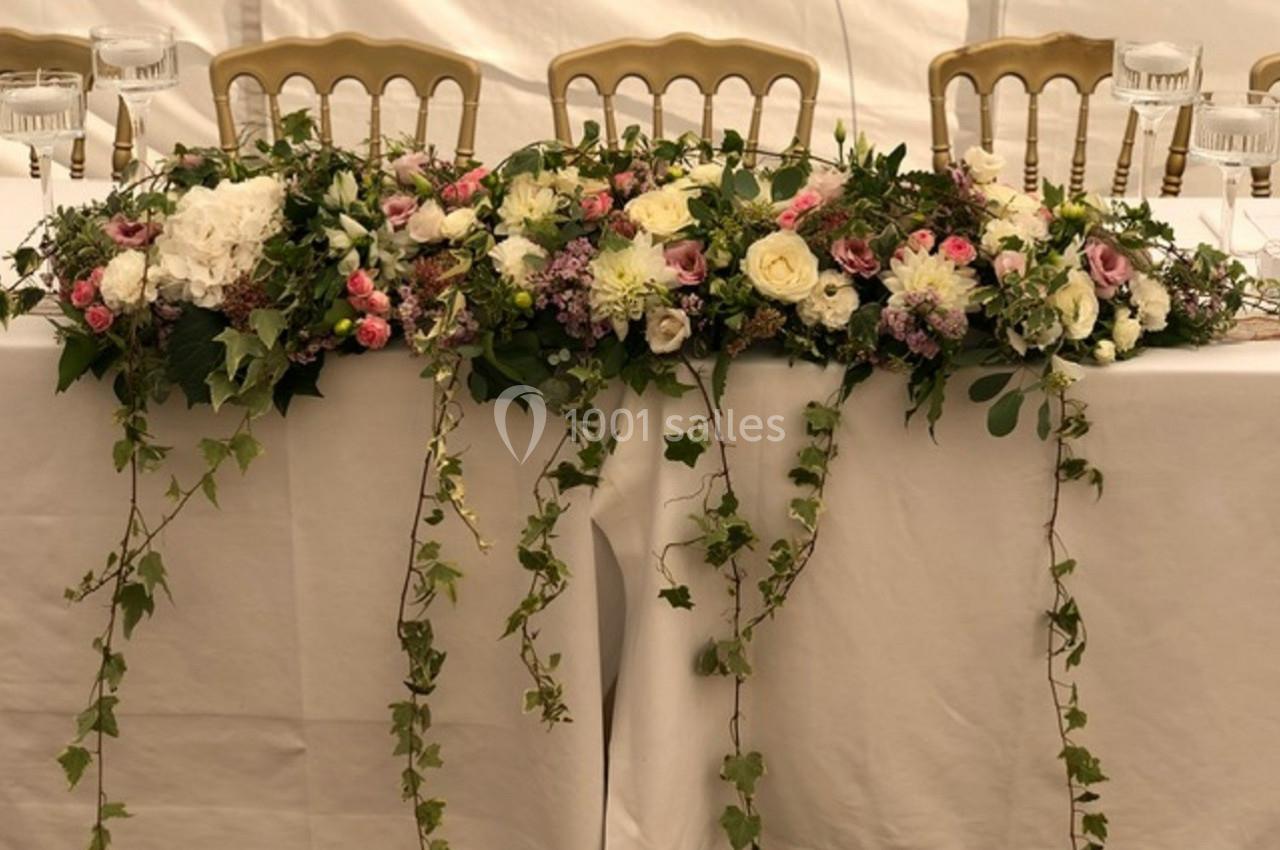 Arrangement floral coloré avec roses, pivoines et feuillage tombant, décorant une table recouverte d'une nappe blanche.