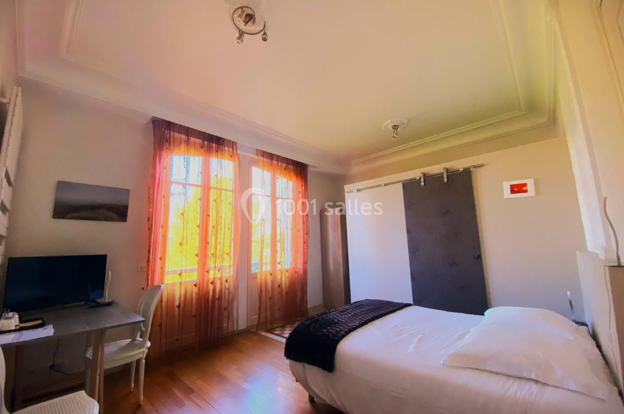 Chambre lumineuse avec lit double, bureau, télévision, rideaux orange et porte coulissante grise.