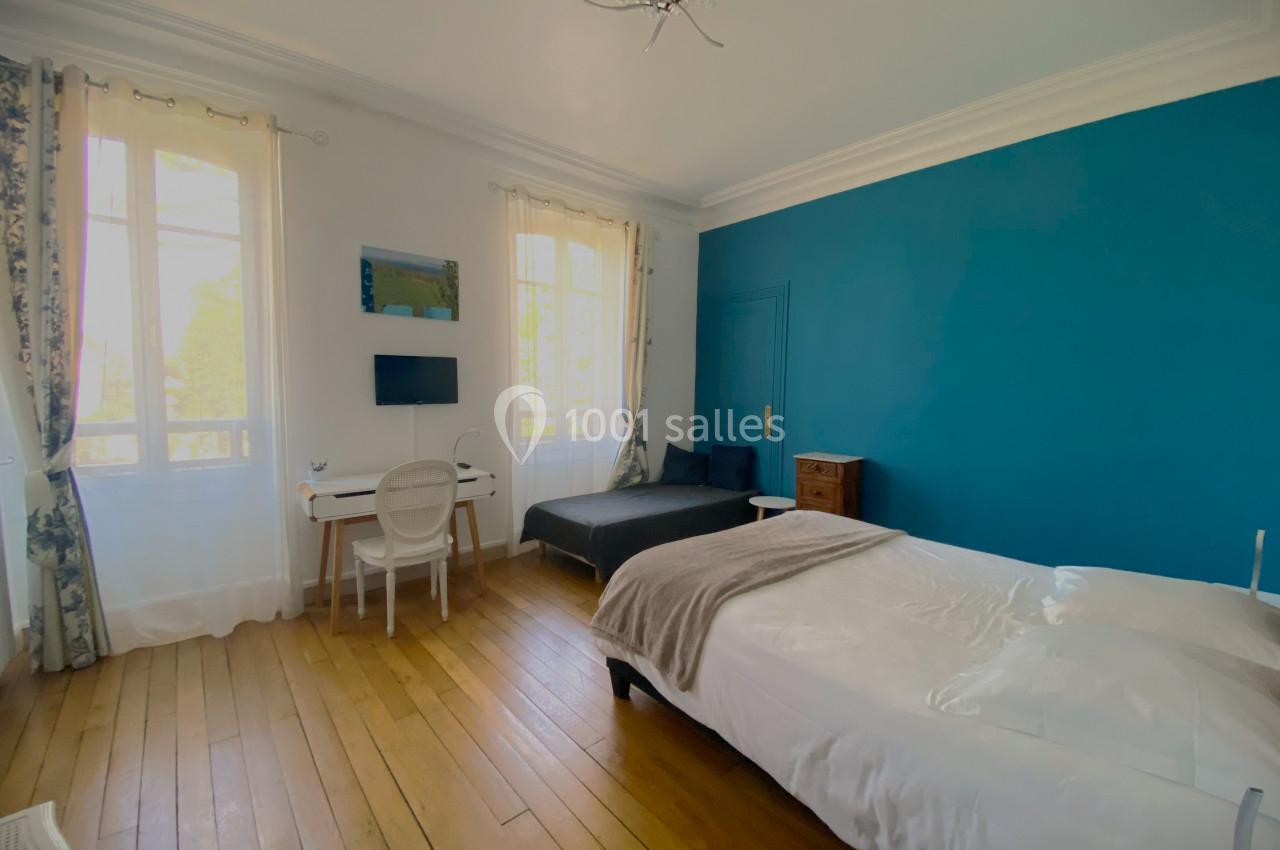 Chambre lumineuse avec mur bleu, lit double, bureau, chaise, canapé et parquet en bois clair.