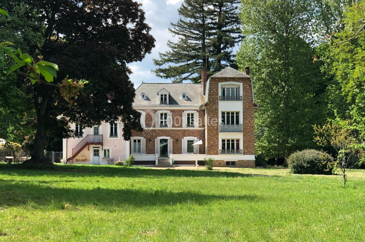 Grande maison en briques rouges entourée d'arbres et d'une pelouse verdoyante sous un ciel partiellement nuageux.