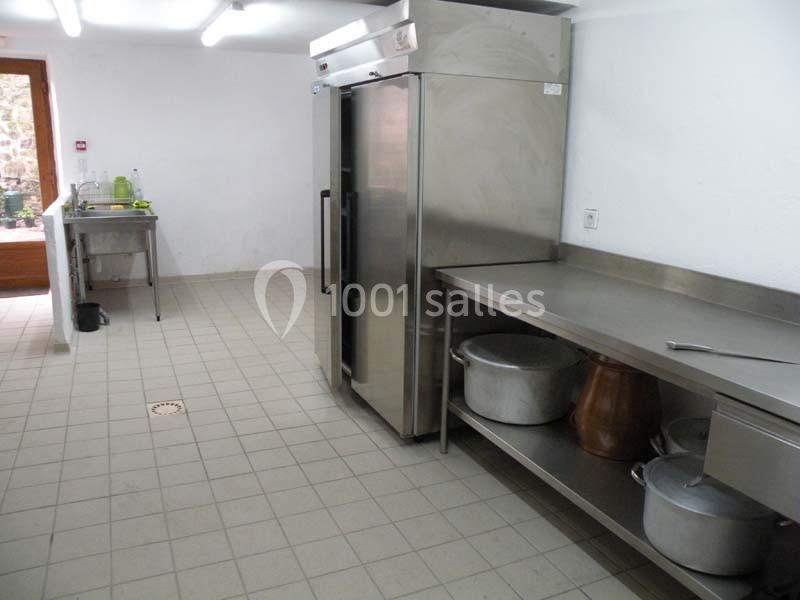 Cuisine professionnelle avec sol carrelé, plan de travail en inox, réfrigérateur et évier en arrière-plan.