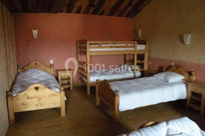 Chambre rustique avec lits simples en bois, lits superposés, murs colorés et plafond en bois incliné.