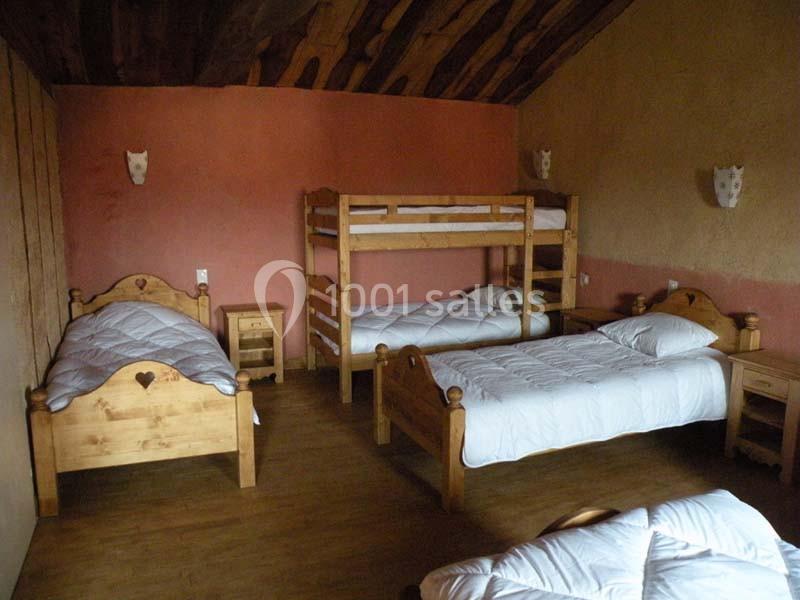 Chambre rustique avec lits simples en bois, lits superposés, murs colorés et plafond en bois incliné.