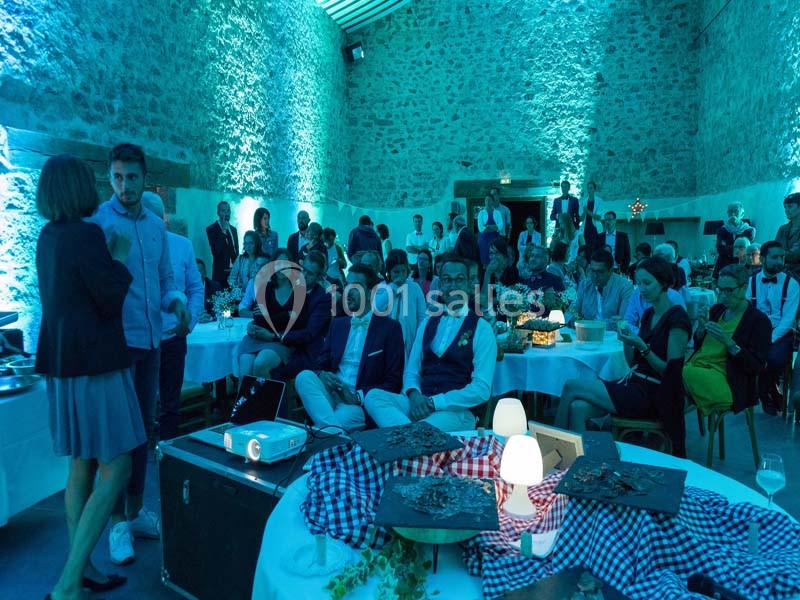 Des invités assis et debout dans une salle en pierre éclairée de lumières bleues, lors d'un événement festif.