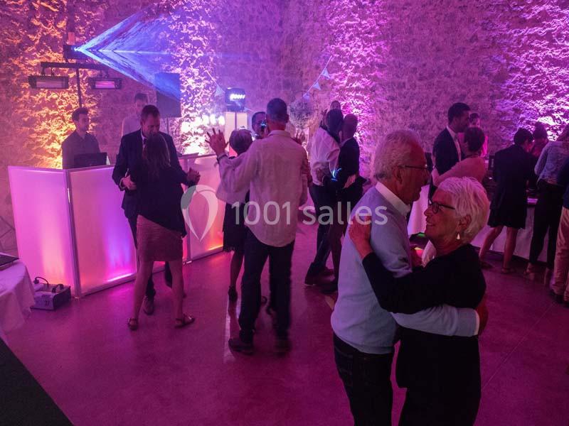 Personnes dansant dans une salle éclairée par des lumières colorées, avec un DJ en arrière-plan.