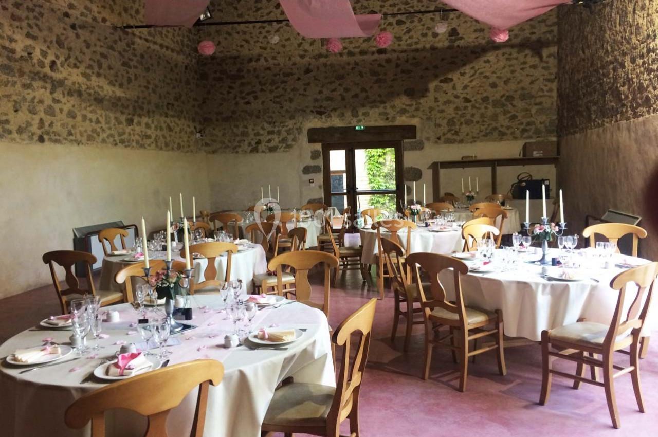 Salle de réception rustique avec tables rondes dressées, décorée de nappes blanches et de touches roses.