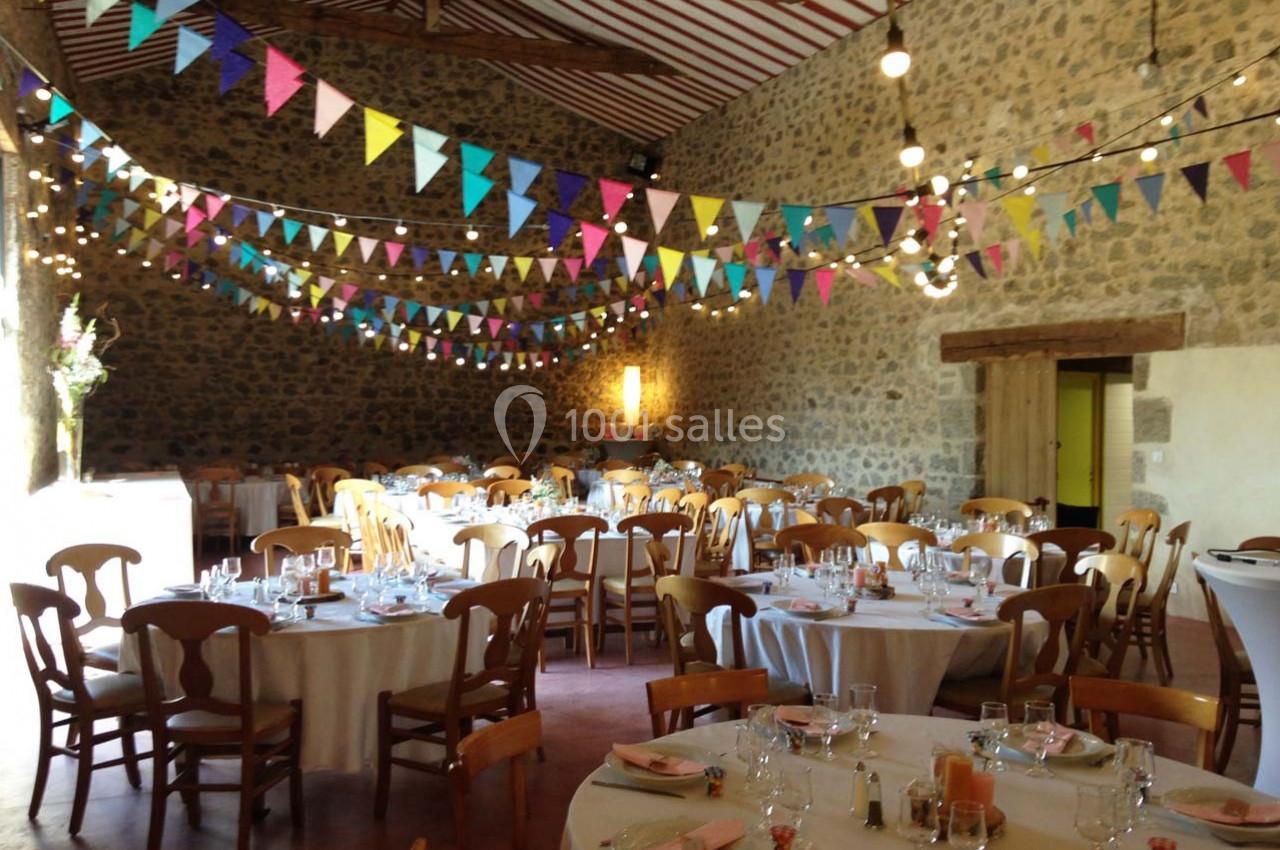 Salle de réception décorée de guirlandes colorées, avec des tables rondes dressées pour un événement festif.