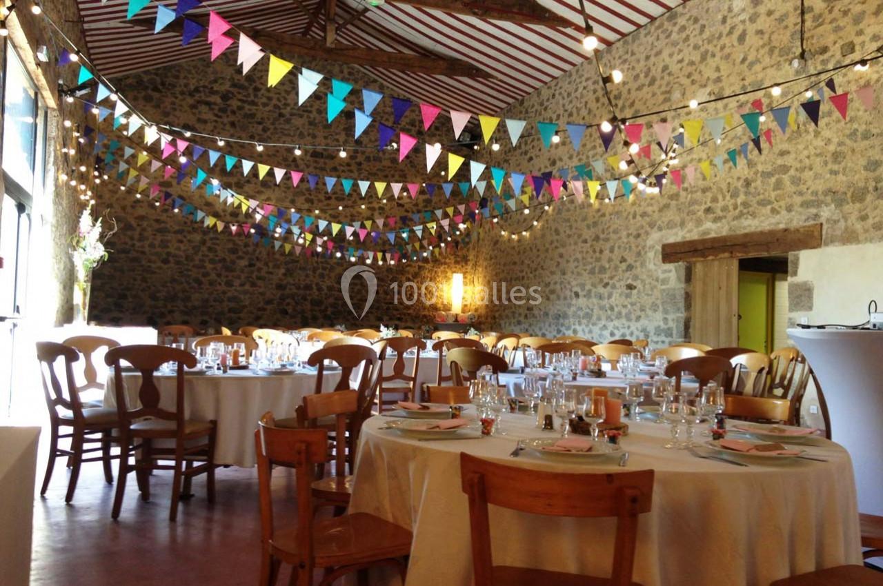 Salle en pierre décorée de guirlandes colorées, tables rondes dressées pour un événement festif.