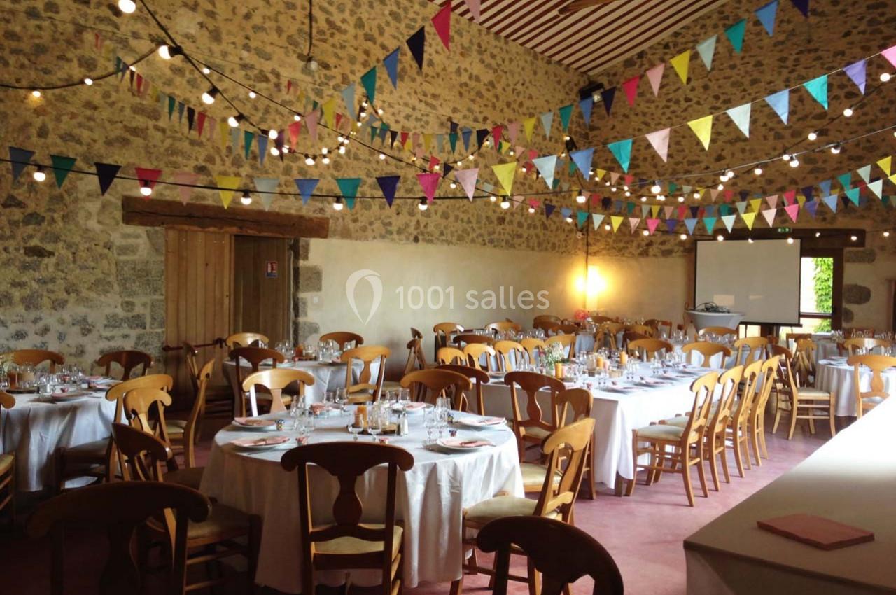 Salle de réception décorée avec des guirlandes colorées et des tables rondes dressées pour un événement.