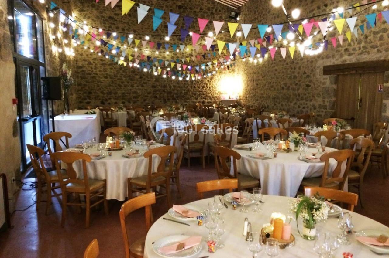 Salle de réception décorée avec des guirlandes colorées, des tables rondes dressées et des chaises en bois.