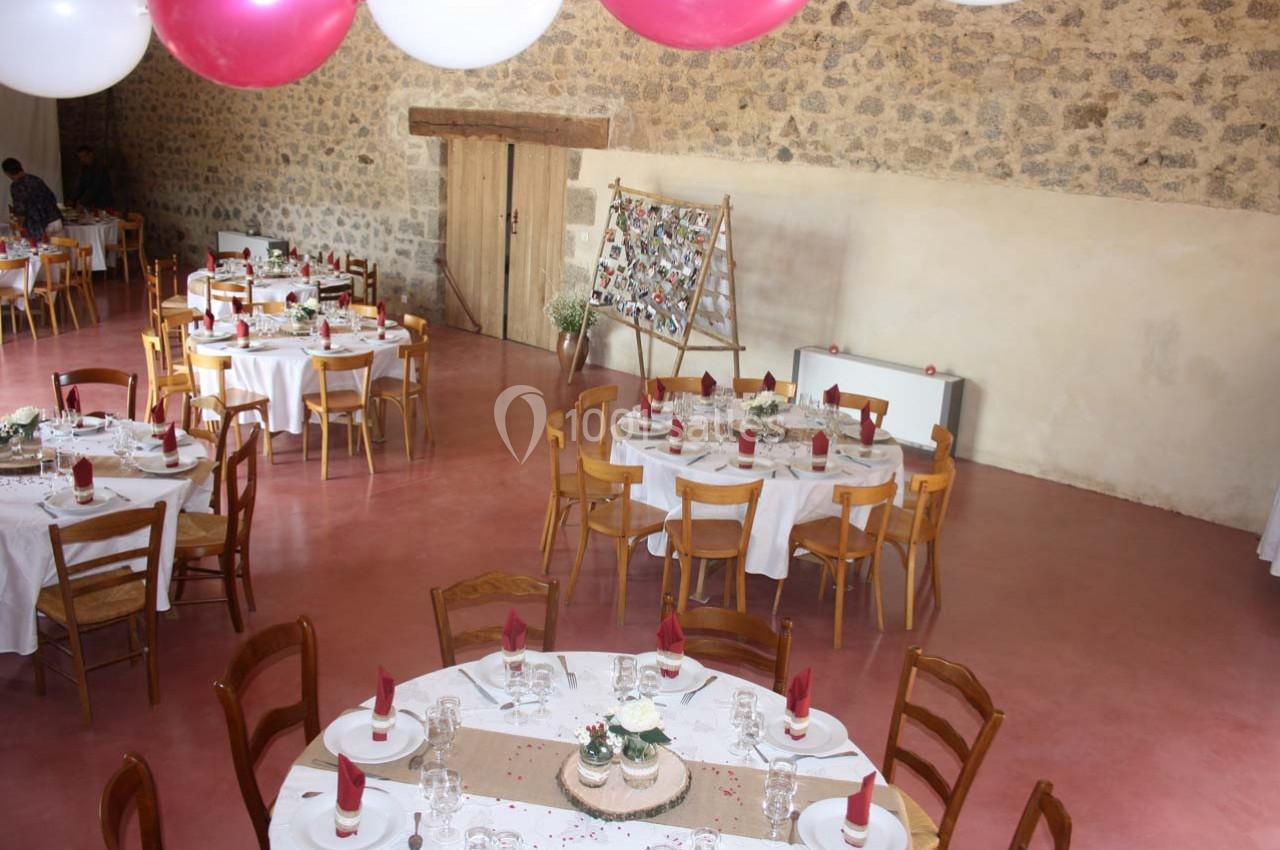 Salle de réception décorée avec des tables rondes dressées, des nappes blanches et des ballons suspendus au plafond.