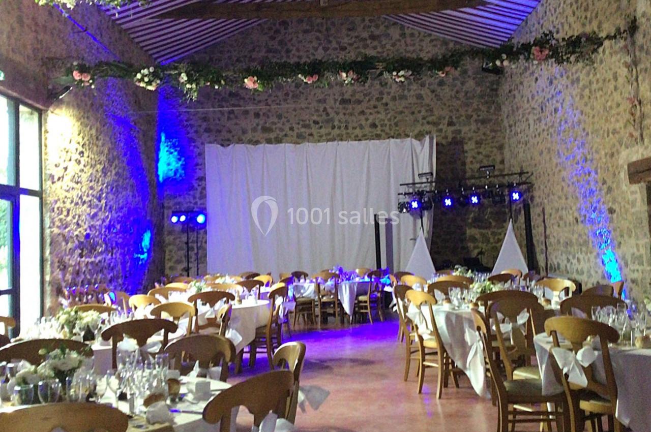 Salle de réception en pierre avec tables décorées pour un événement, éclairage bleu et guirlandes florales suspendues.