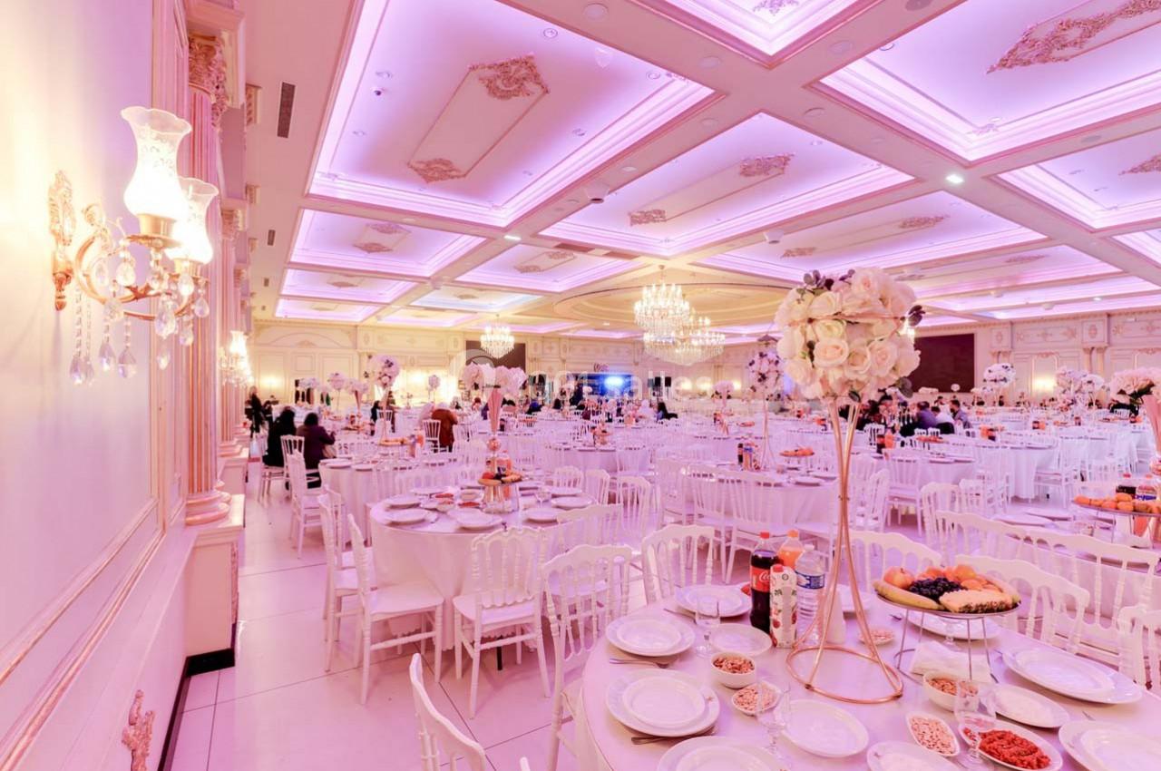 Salle de réception élégante décorée de tons roses et blancs, avec tables dressées et éclairage chaleureux.