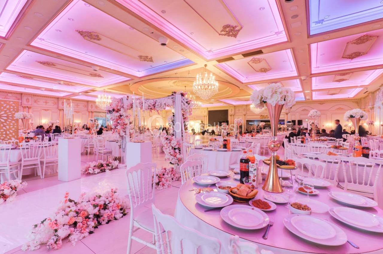 Salle de réception décorée avec des fleurs roses, tables dressées et éclairage rose chaleureux.