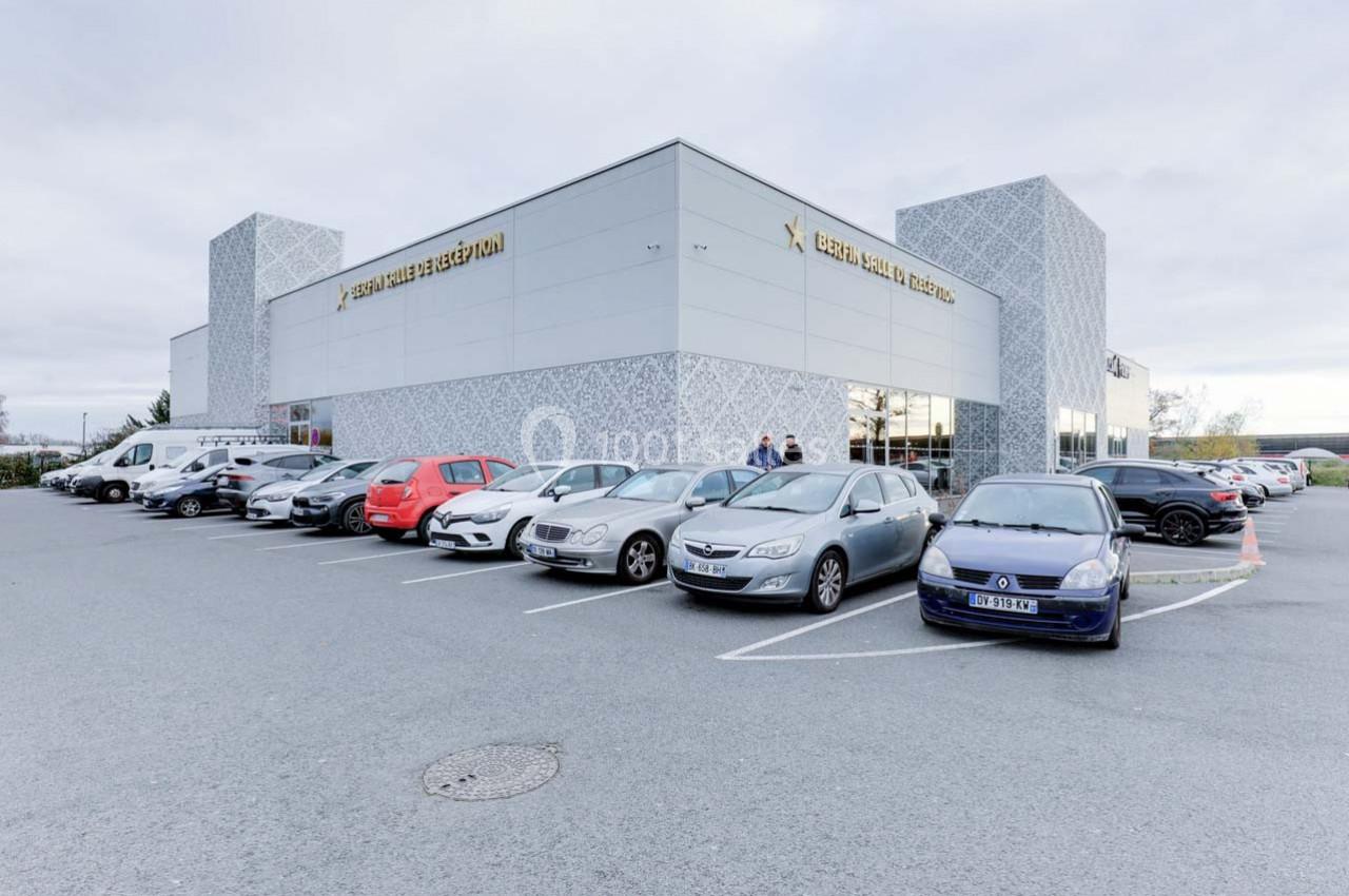Parking avec plusieurs voitures devant un grand bâtiment moderne aux façades claires et décoratives.