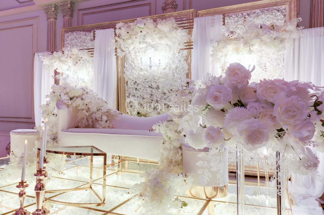 Décor de mariage élégant avec canapé blanc, fleurs blanches abondantes et bougies sur un sol en verre réfléchissant.