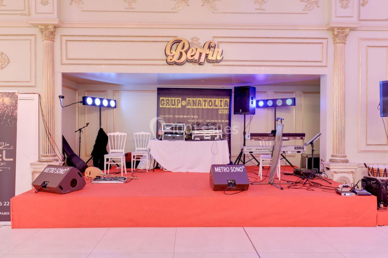 Scène intérieure avec équipements audio, éclairages, instruments et une bannière du groupe ’Grup Anatolia’.