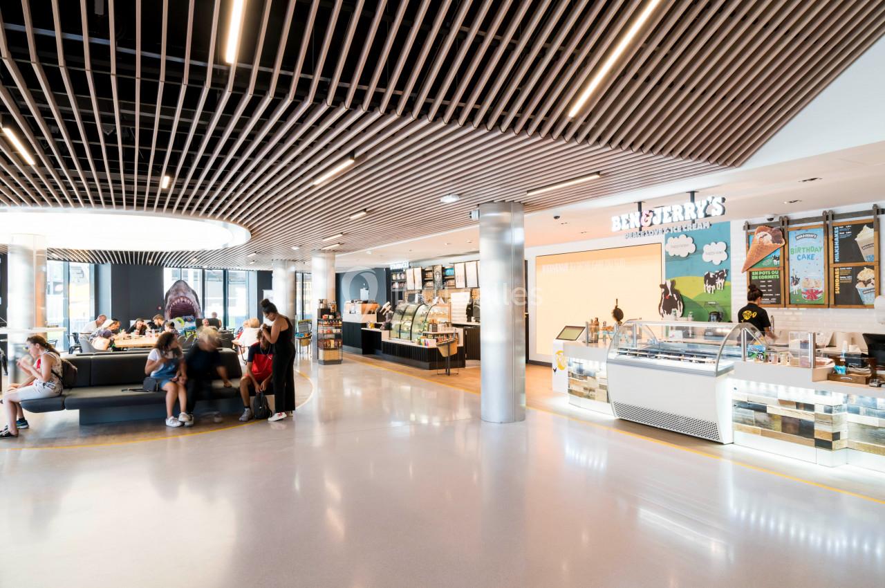 Intérieur lumineux d'une boutique avec comptoir de glaces, présentoirs et clients assis ou en file d'attente.