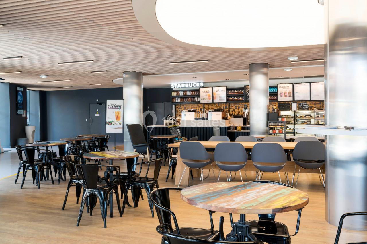 Intérieur d'un café moderne avec tables en bois, chaises noires et comptoir de service en arrière-plan.
