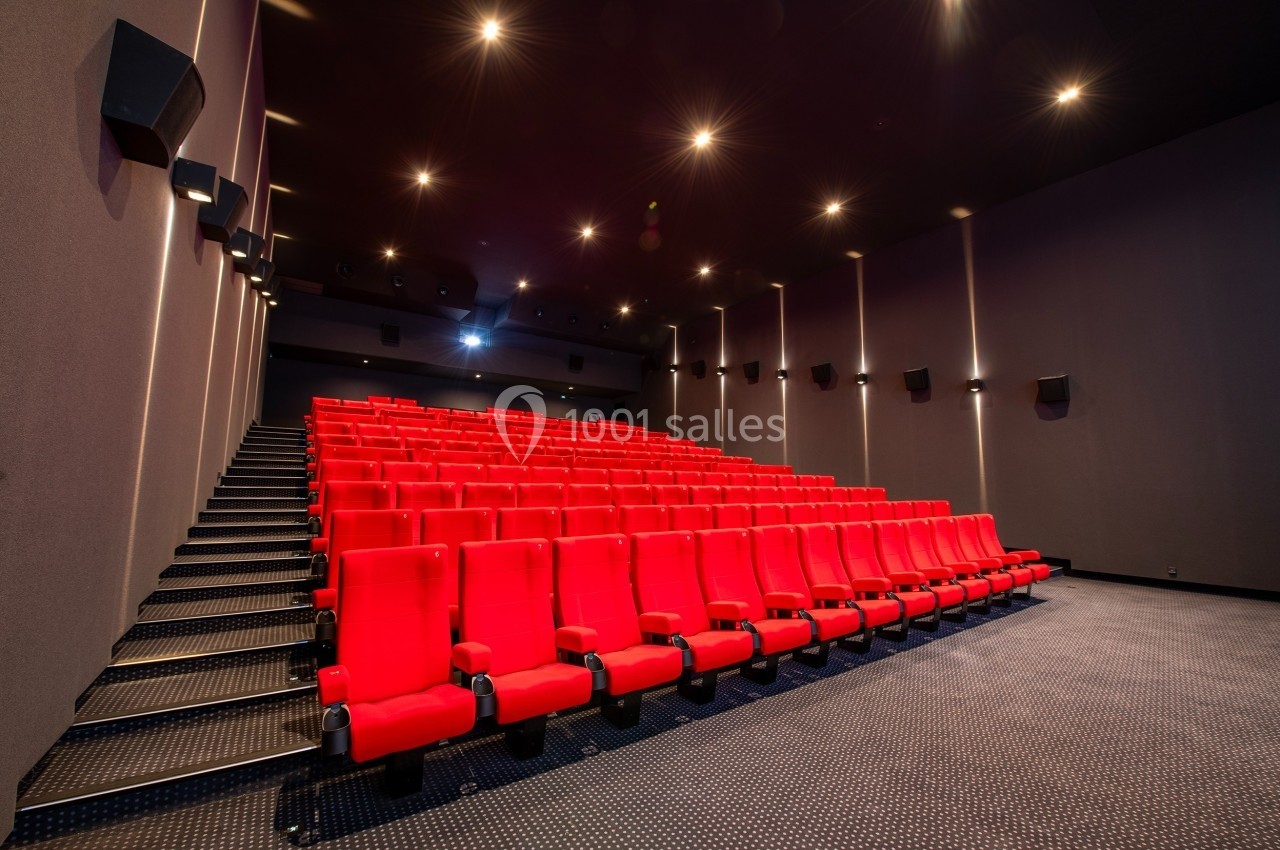 Salle de cinéma vide avec des rangées de sièges rouges et un éclairage tamisé.