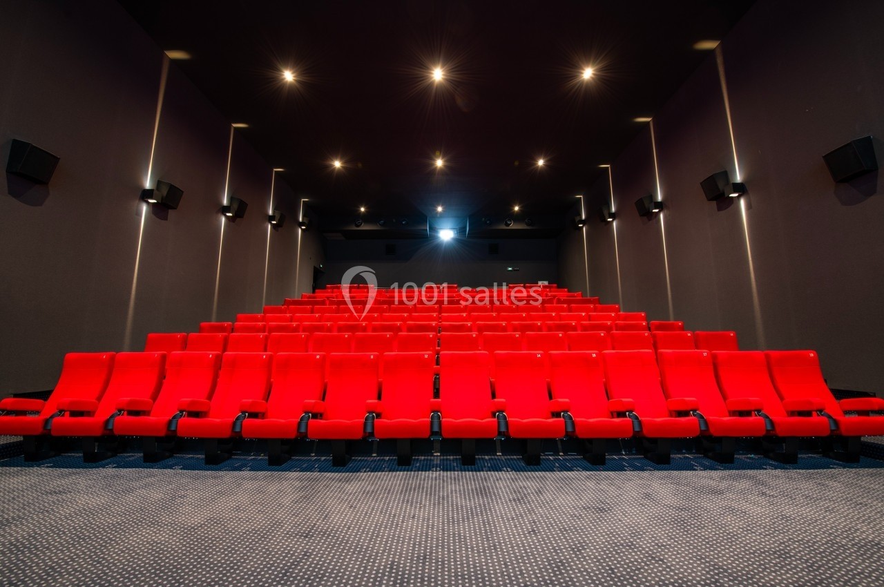 Salle de cinéma vide avec des rangées de fauteuils rouges alignés face à un écran blanc.
