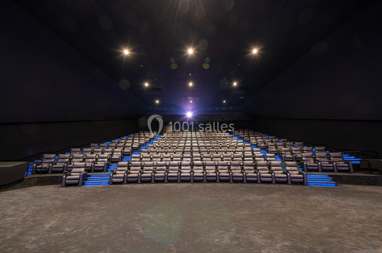 Salle de cinéma vide avec des rangées de sièges inclinables et un éclairage tamisé dirigé vers l'écran.