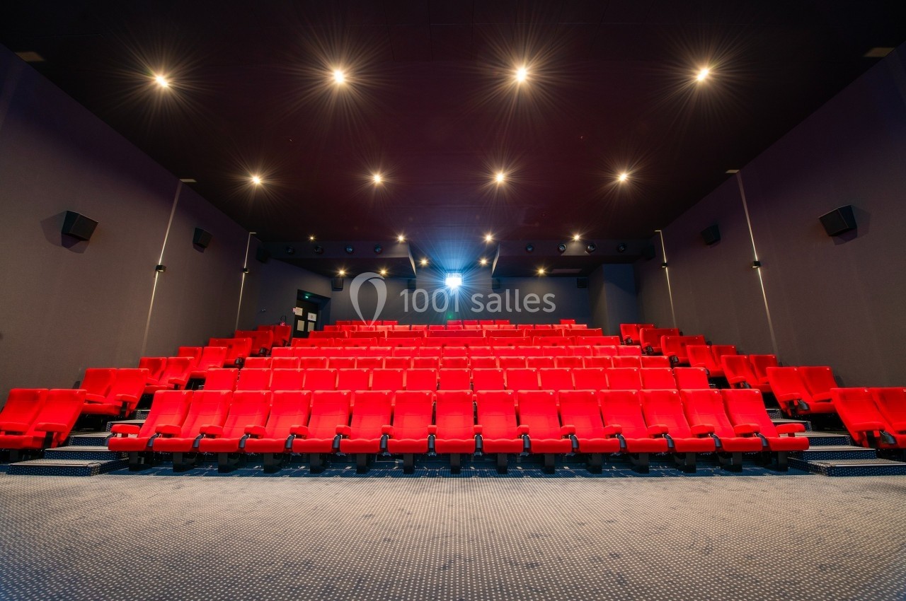 Salle de cinéma vide avec des rangées de sièges rouges, éclairée par des spots au plafond.