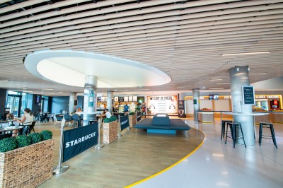 Terrasse d'un café Starbucks devant un immeuble moderne aux façades blanches et jaunes, sous un ciel partiellement nuageux.