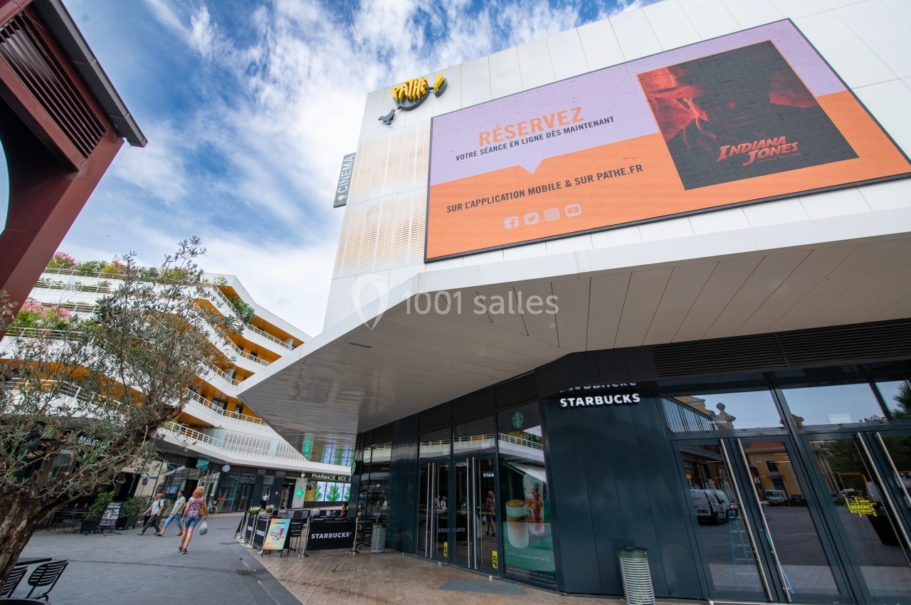 Façade d'un cinéma avec un écran publicitaire affichant une promotion pour un film, devant une terrasse de café.