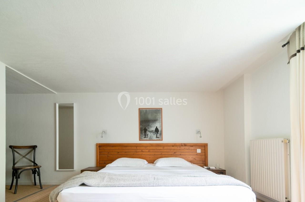 Chambre lumineuse avec un lit double, une tête de lit en bois, une chaise et un tableau au mur.