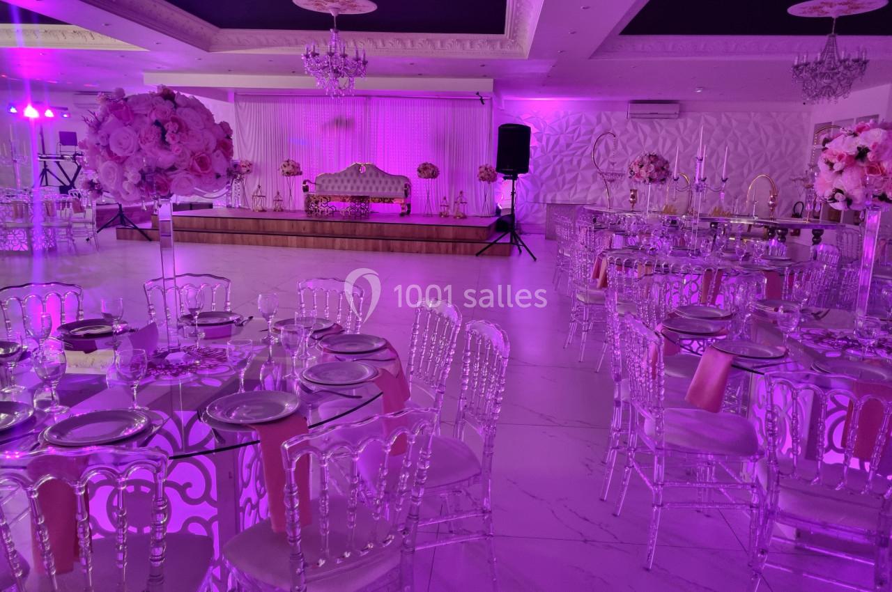 Salle de réception décorée avec des tables dressées, des chaises transparentes et un éclairage rose.