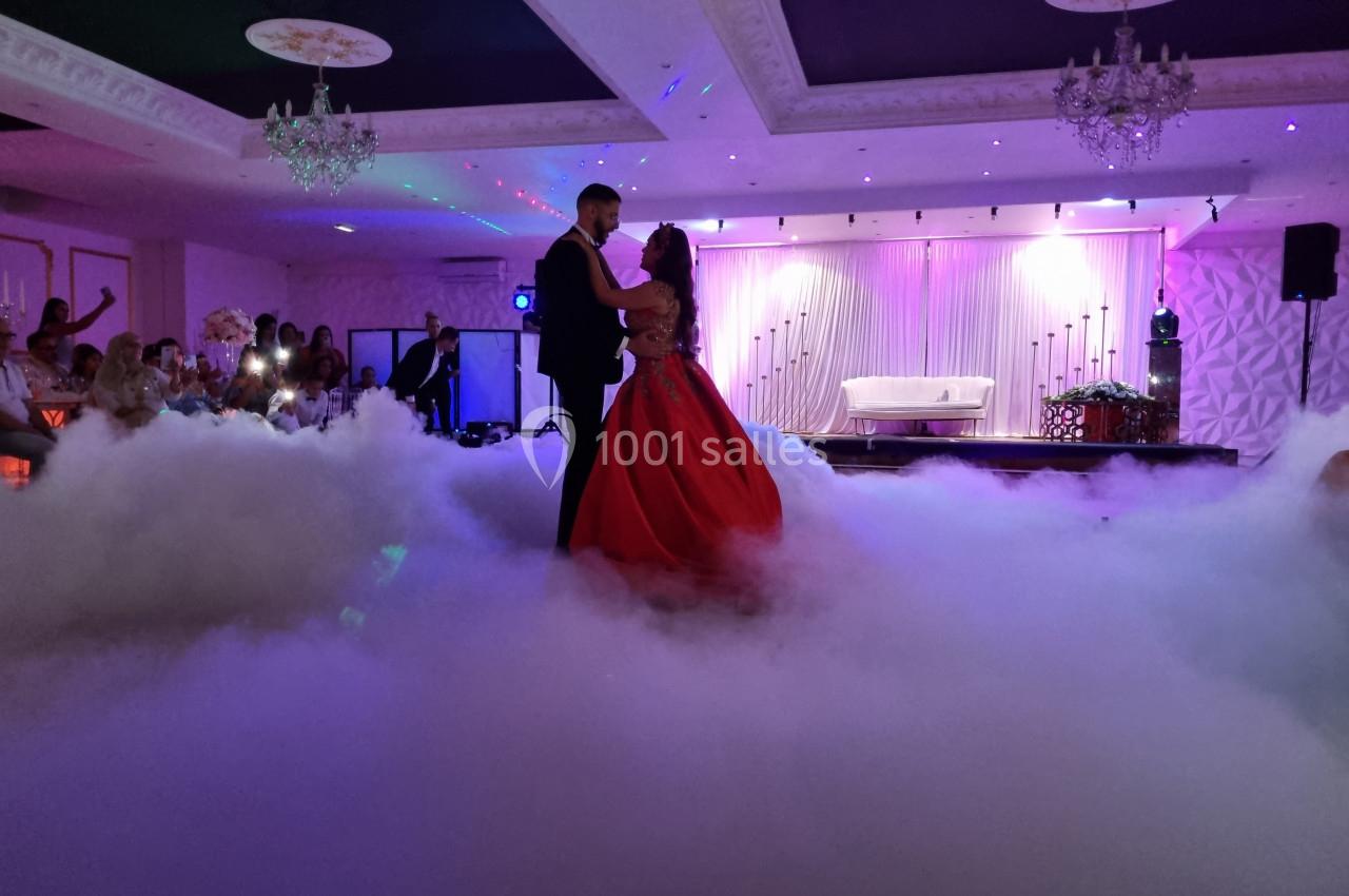 Un couple danse sur une piste entourée de fumée, sous des lumières tamisées dans une salle de réception élégante.
