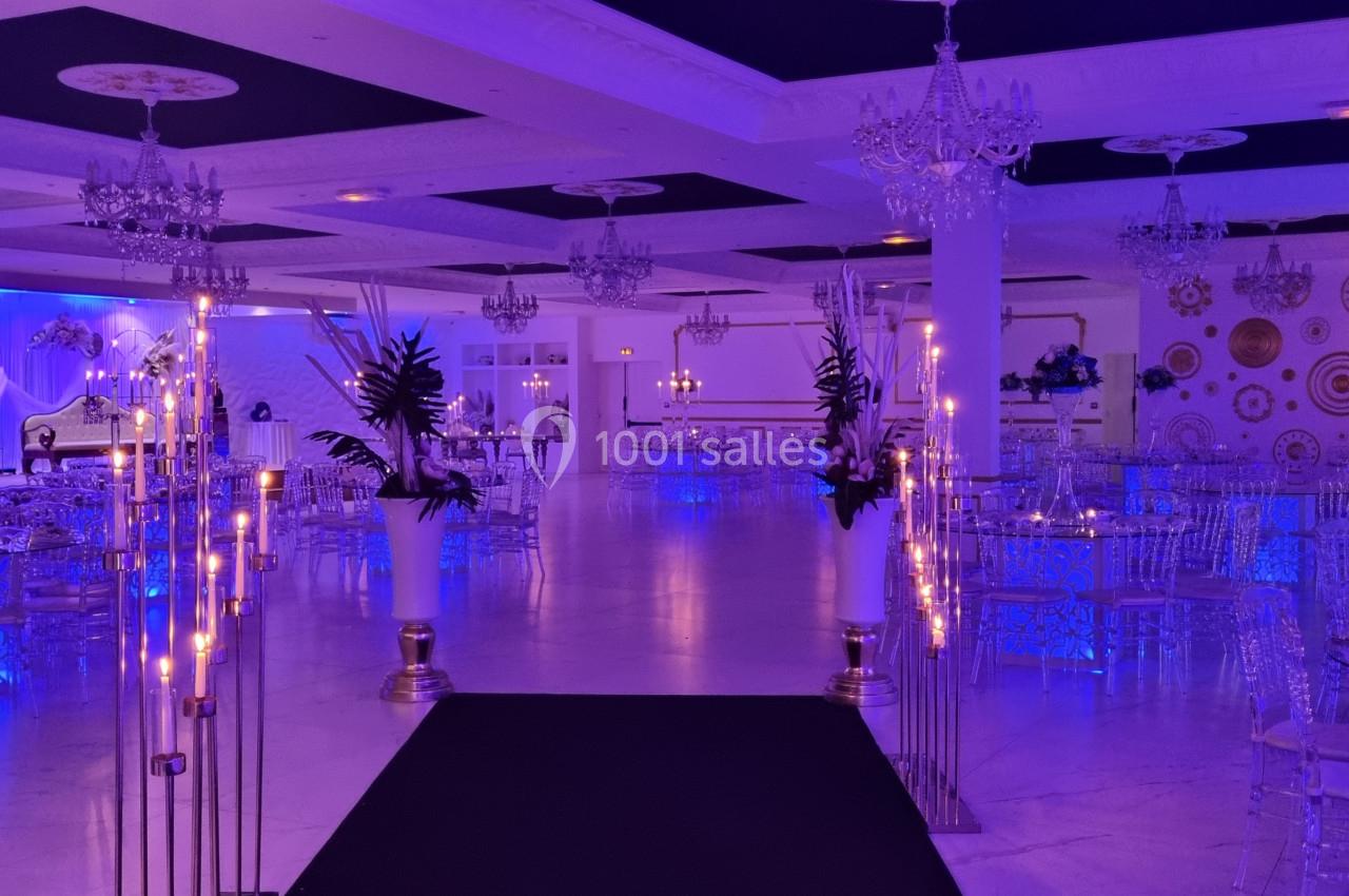 Salle de réception élégante éclairée en bleu, avec tables dressées, chandeliers et décorations murales dorées.
