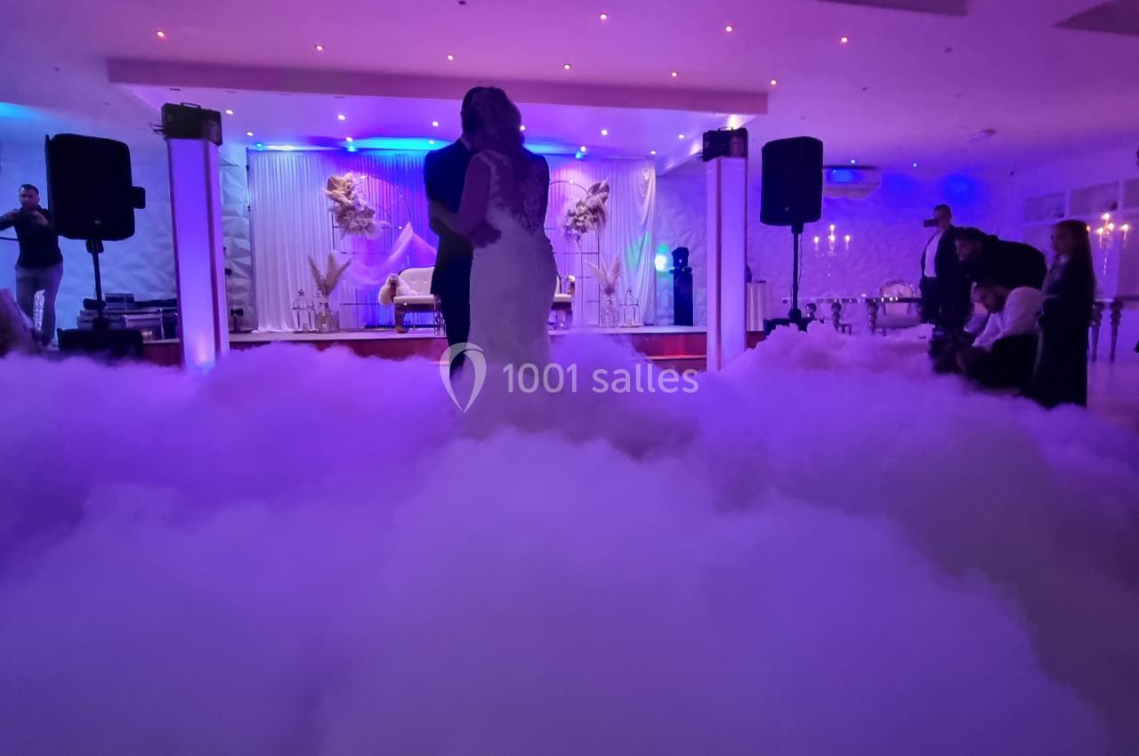 Un couple danse dans une salle de réception éclairée de lumières colorées, entouré d'un effet de fumée au sol.