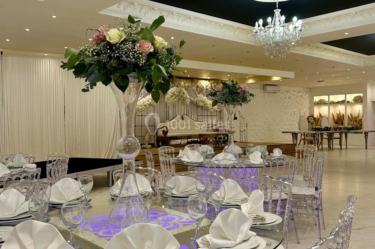 Salle de réception élégante avec tables rondes décorées de nappes blanches, chaises transparentes et centres de table…