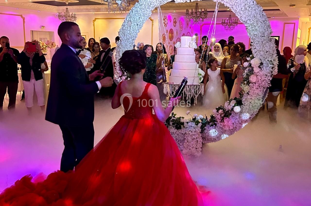 Un couple en tenue de soirée observe un gâteau suspendu dans un cadre floral lors d'une réception festive.