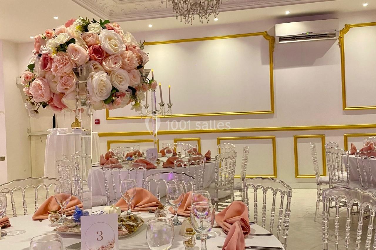 Salle de réception élégante avec tables décorées de nappes blanches, serviettes roses et centre de table floral.