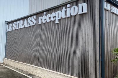 Façade éclairée d'un bâtiment avec l'enseigne lumineuse ’Le Strass réception’ visible de nuit.