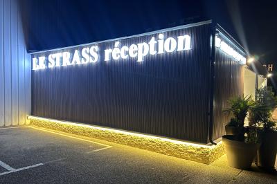 Façade éclairée d'un bâtiment avec l'enseigne lumineuse ’Le Strass réception’ visible de nuit.