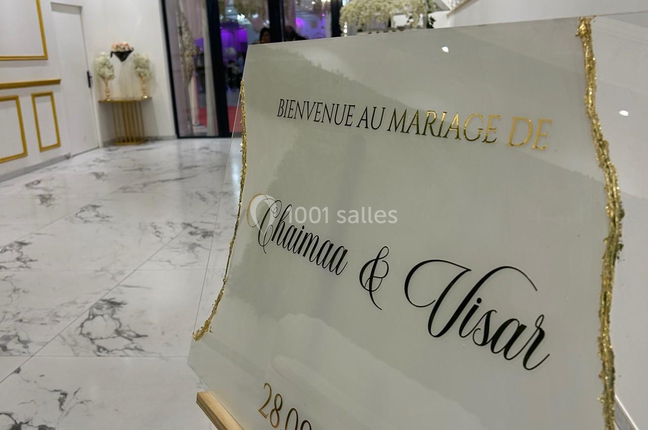 Panneau de bienvenue pour un mariage, placé dans une salle élégante avec décorations blanches et dorées.