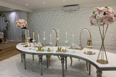 Table de mariage décorée de fleurs blanches et roses, avec deux chaises et un panneau ’Mr & Mrs’ au centre.