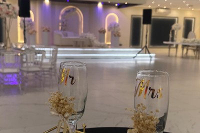 Table de mariage décorée de fleurs blanches et roses, avec deux chaises et un panneau ’Mr & Mrs’ au centre.