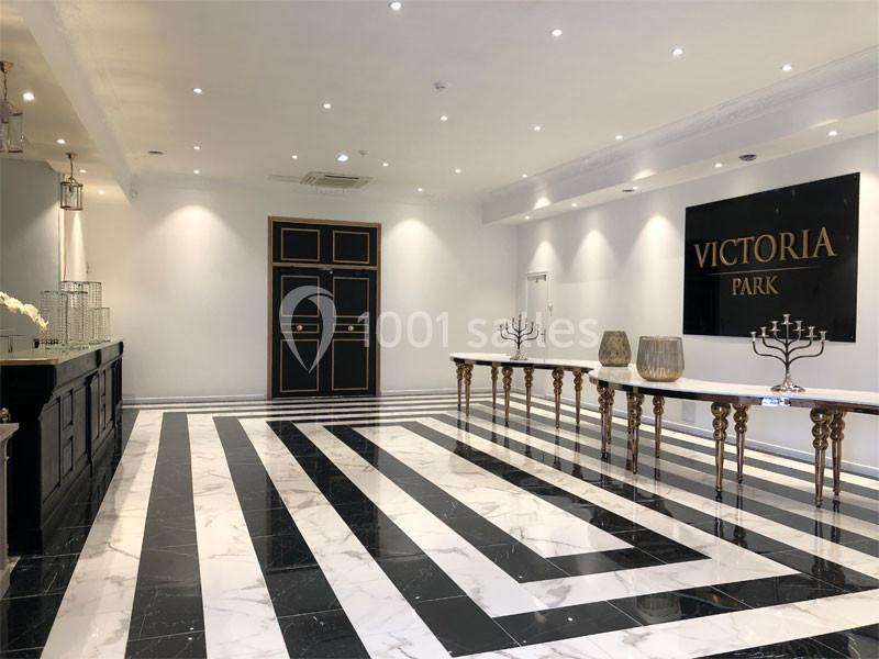 Salle lumineuse avec sol en marbre noir et blanc, comptoirs élégants et panneau ’Victoria Park’ sur le mur.
