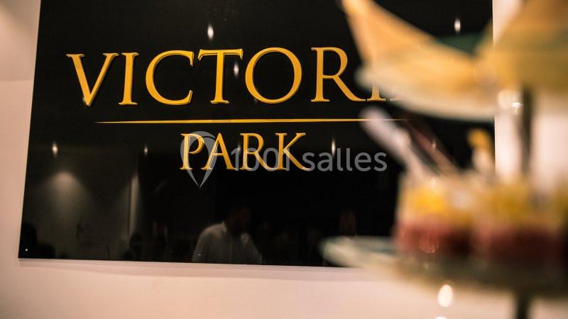 Enseigne noire avec le texte ’Victoria Park’ en lettres dorées, floue en arrière-plan d'un présentoir de desserts.