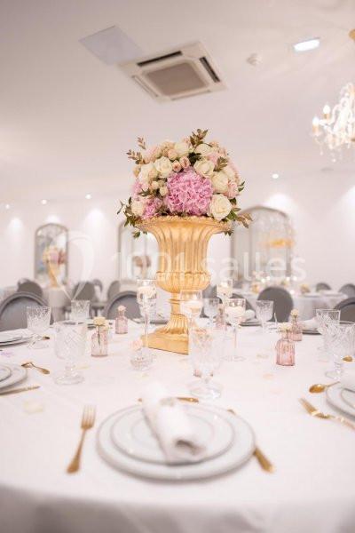 Centre de table floral avec des roses et des hortensias dans un vase doré, entouré de vaisselle élégante sur une table…