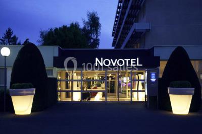 Chambre avec un lit double, un canapé gris, un mur clair et un tableau encadré.