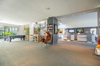 Chambre avec un lit double, un canapé gris, un mur clair et un tableau encadré.