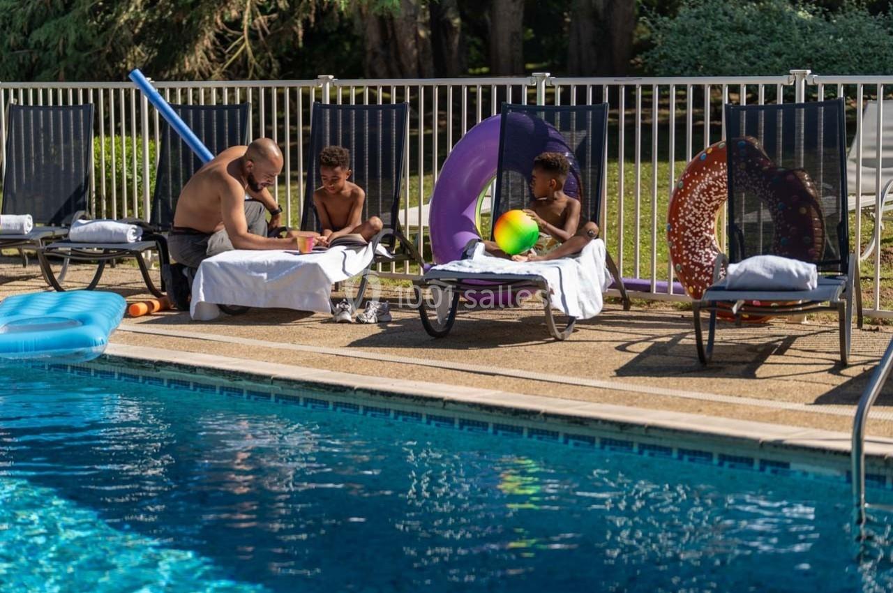 Un homme et deux enfants assis sur des transats près d'une piscine, entourés de jouets et de bouées colorées.